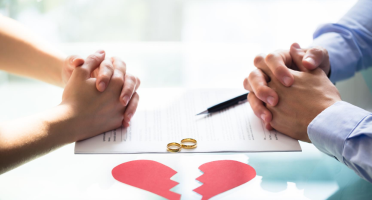 Two people with clasped hands across a table with a hear that has been broken in-between them.