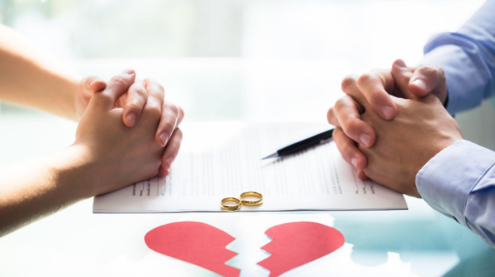 Two people with clasped hands across a table with a hear that has been broken in-between them.